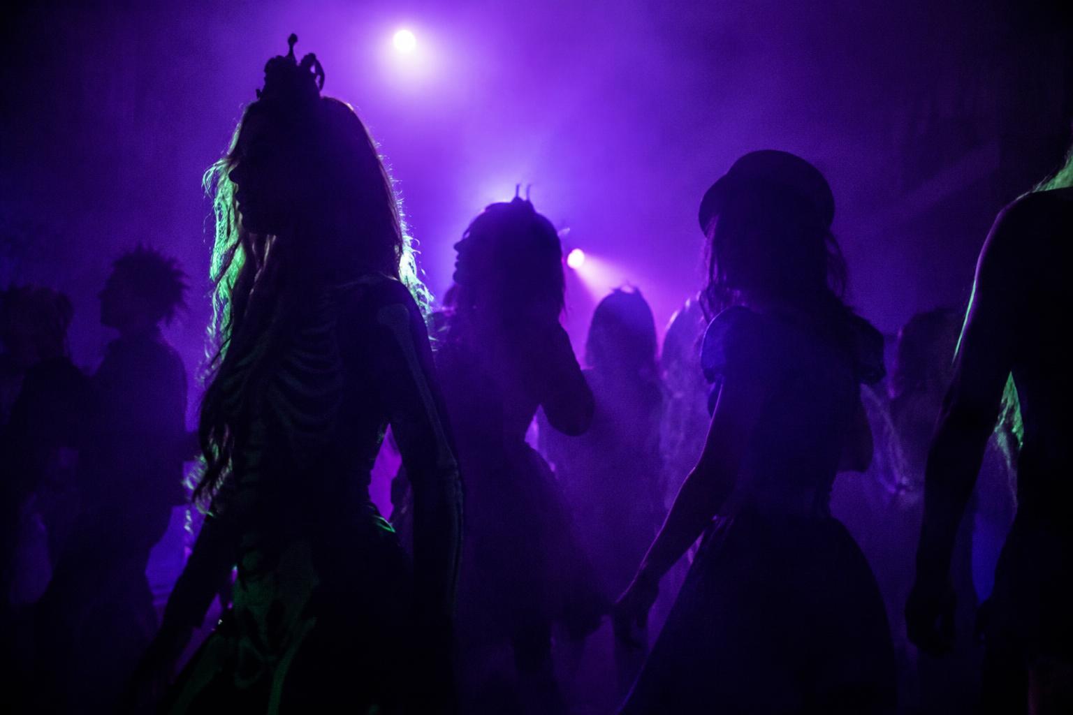 Silhouetted crowd in fancy dress under ultraviolet light